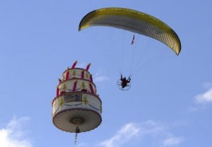 a paraglider flies around a cake shape balloon