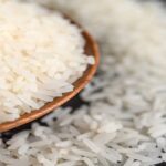 Milled rice in a bowl and a wooden spoon on the black cement floor. Selective focus
